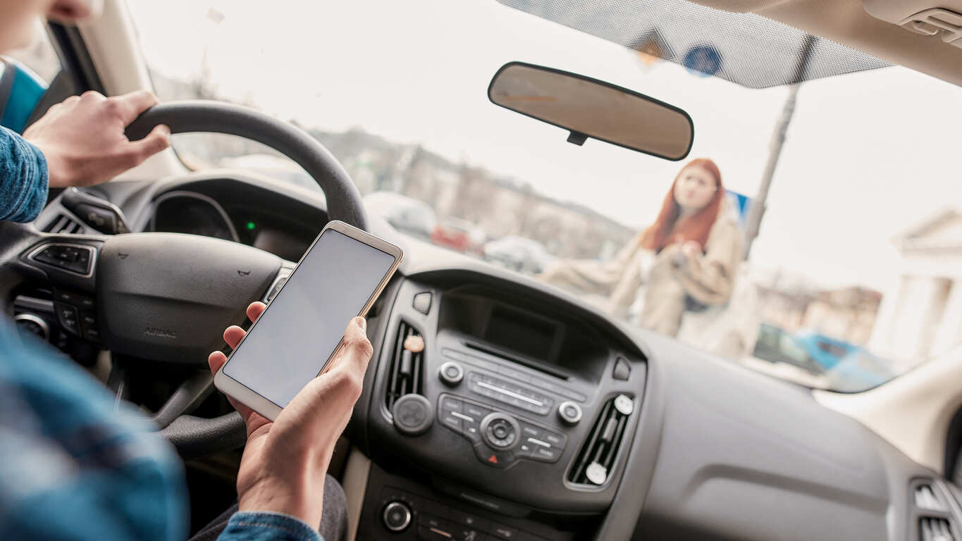 Inside view of a car showing a driver looking at a phone instead of the road, symbolizing the dangers of distracted driving and its relevance in personal injury cases.
