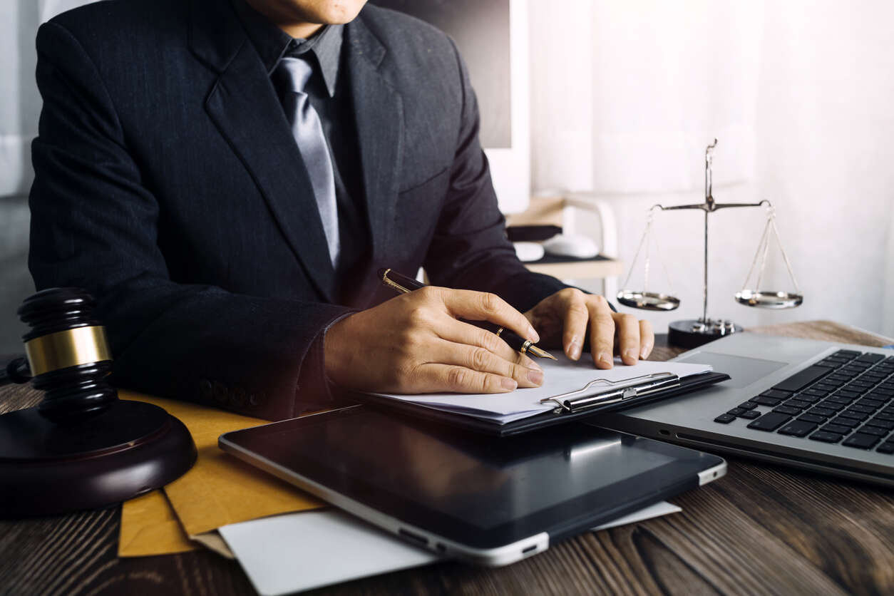 A lawyer in a suit reviewing legal documents at a desk with a gavel, scales of justice, and laptop, representing a San Diego train accident lawyer