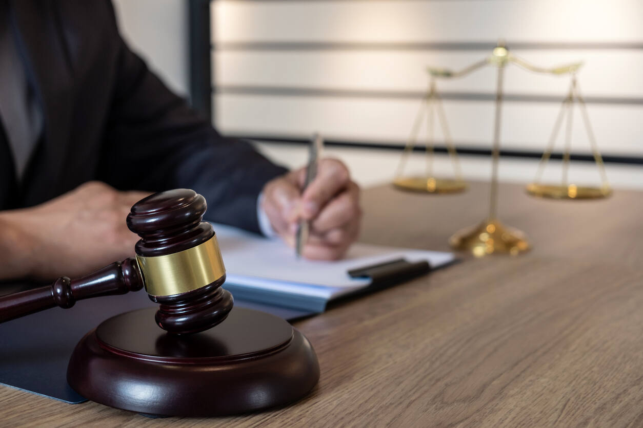 Lawyer writing on a document , gavel and scale of justice on the table. representing scale of justice.