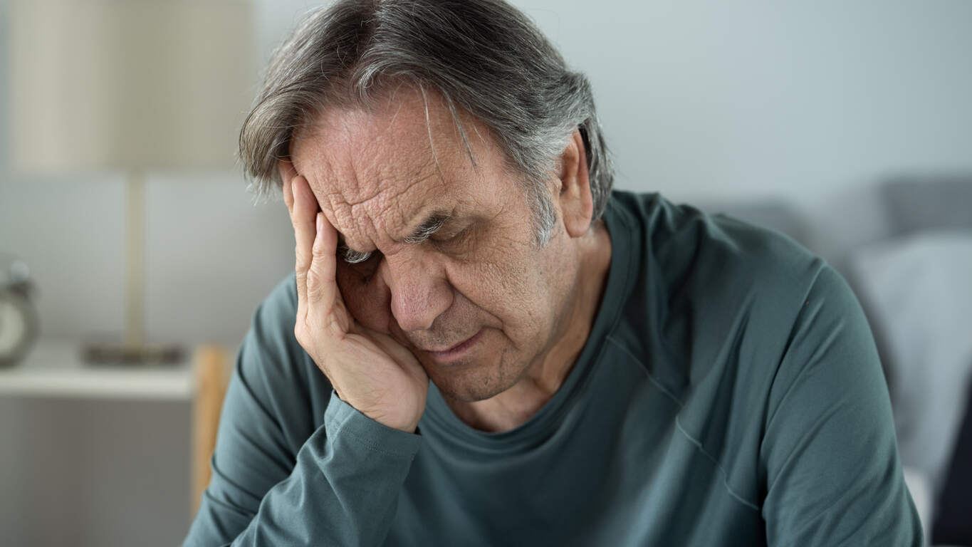 An elderly man with a pained expression holds his hand to his head, symbolizing the suffering caused by nursing home abuse and the need for legal representation from attorneys in San Diego.