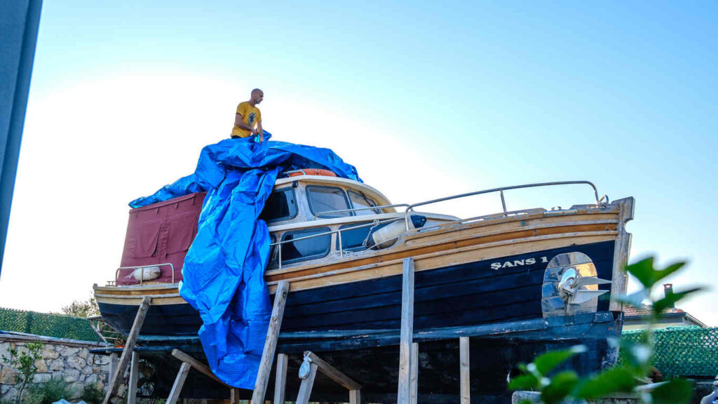 A man standing on a boat covered with a blue tarp on dry dock, symbolizing boat owner liability for injuries.