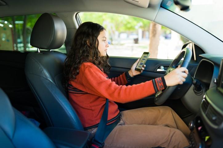 Teenage girl texting or using an app while driving a car, a clear example of distracted driving behavior.